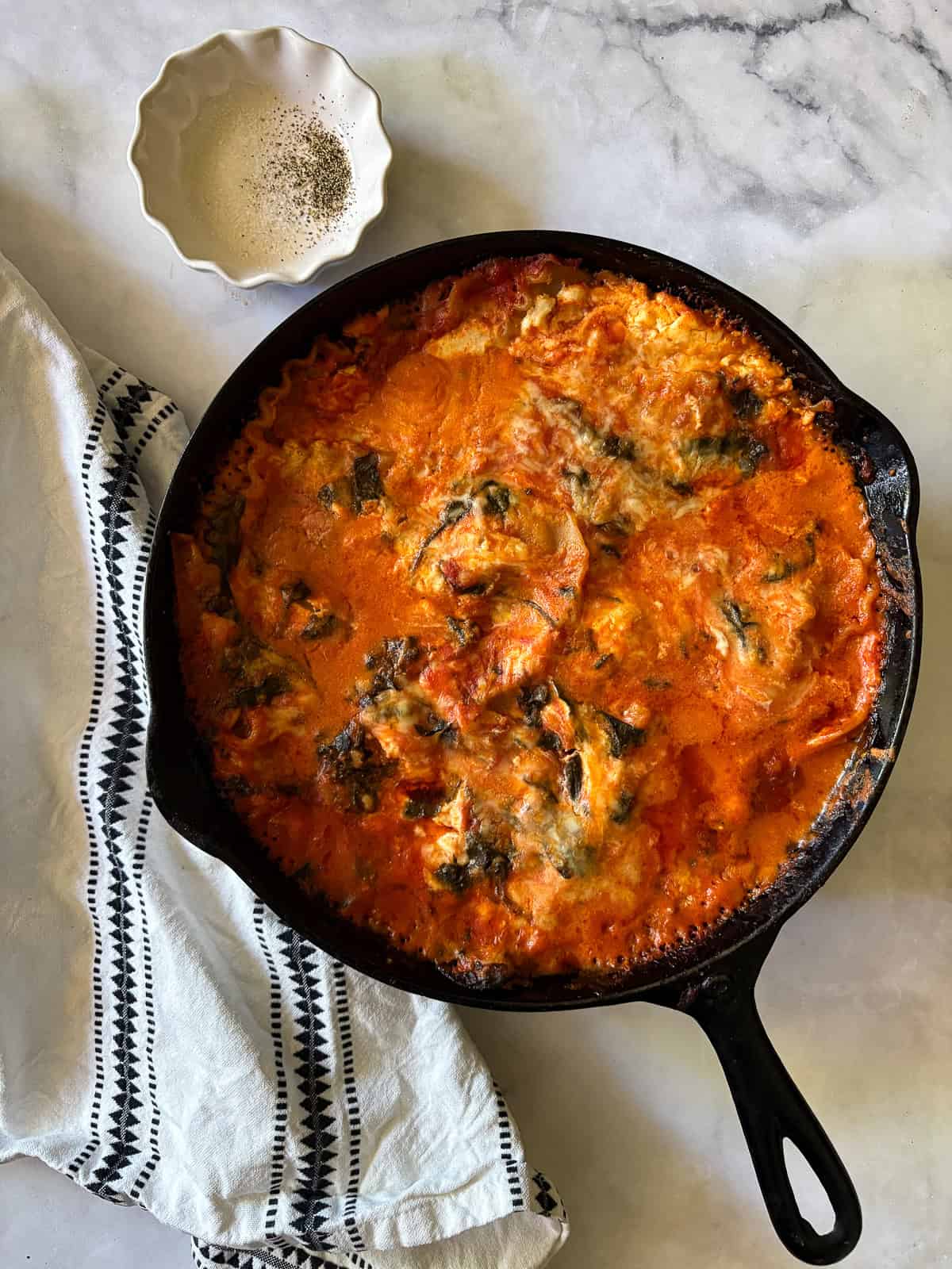 A baked pan of gluten free skillet lasagna next to a napkin and a dish of salt and pepper for seasoning.