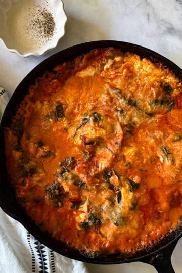 A baked pan of gluten free skillet lasagna next to a napkin and a dish of salt and pepper for seasoning.