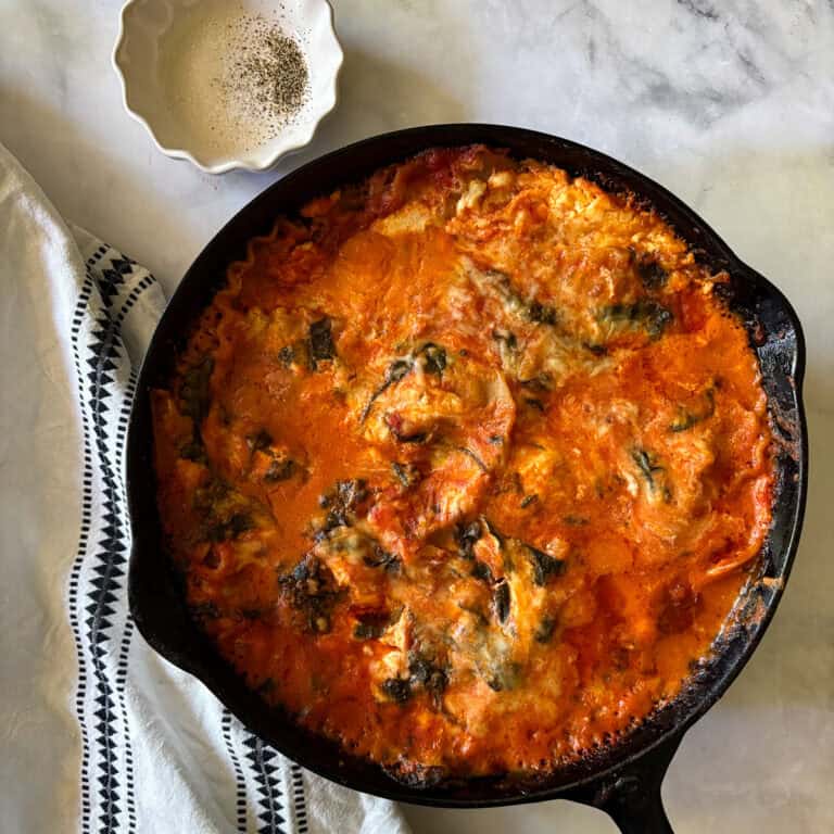 A baked pan of gluten free skillet lasagna next to a napkin and a dish of salt and pepper for seasoning.