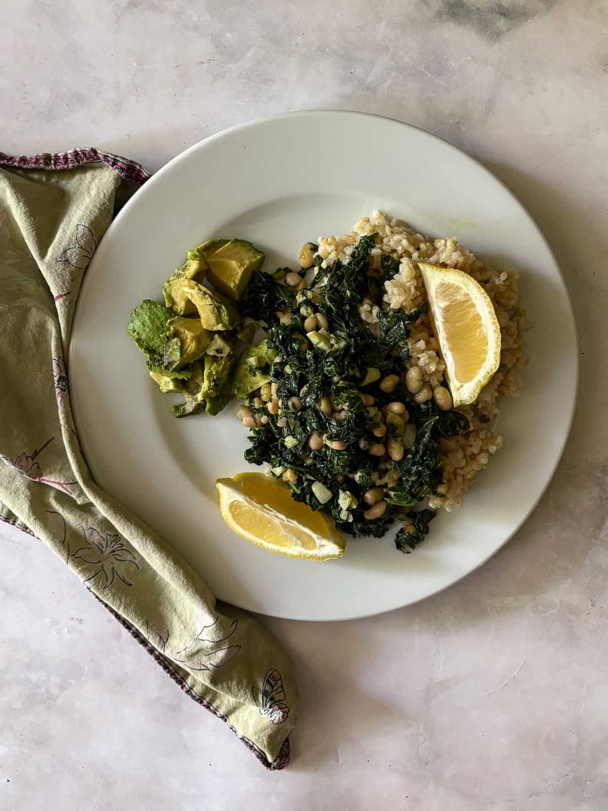 Garlicky white beans and kale are brightened up with lemon juice for a simple, satisfying, and QUICK vegetarian main. White beans and kale with lemon wedges on a plate with a napkin next to it.