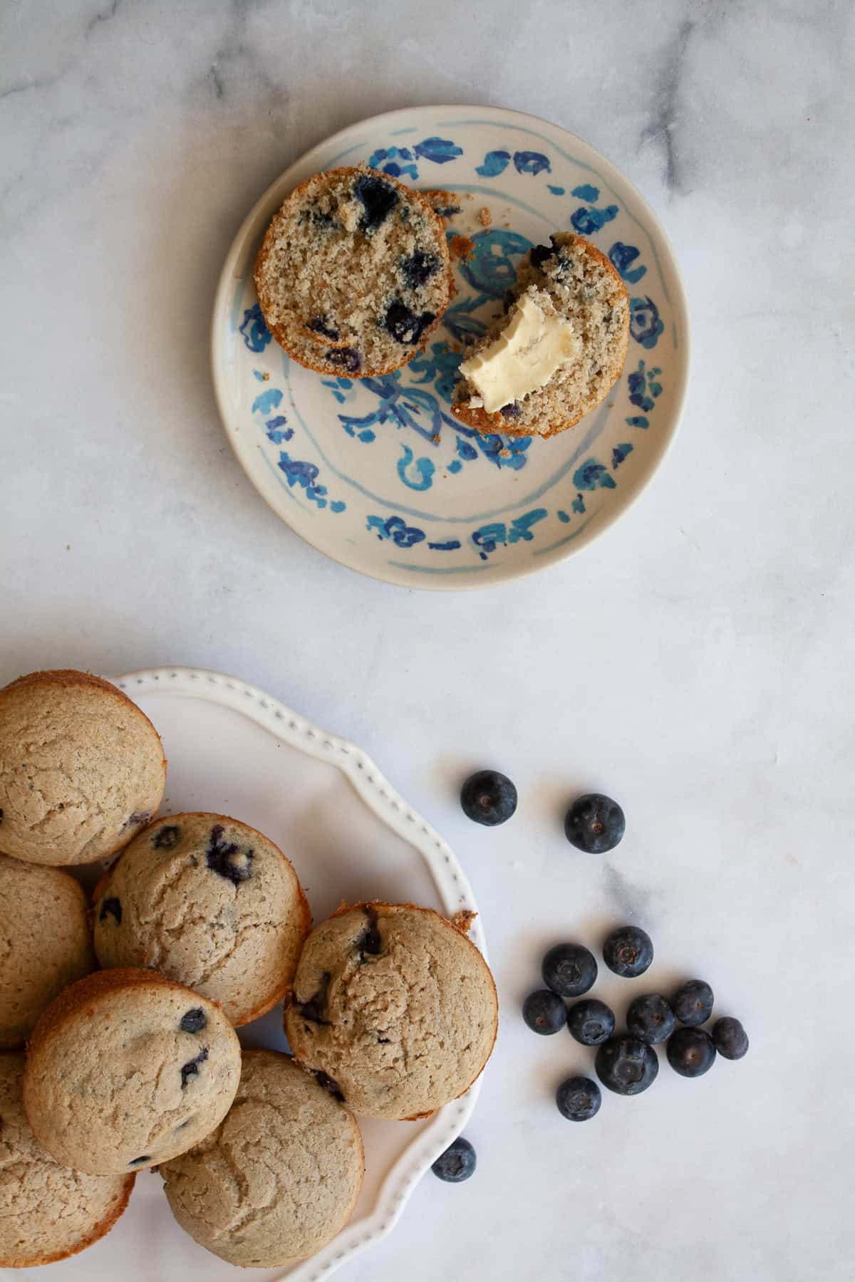 These heart-healthy whole wheat blueberry muffins are a family favorite, made with loads of juicy berries and sweetened with maple syrup. A whole wheat blueberry muffin on a plate wit butter and a plate of muffins.