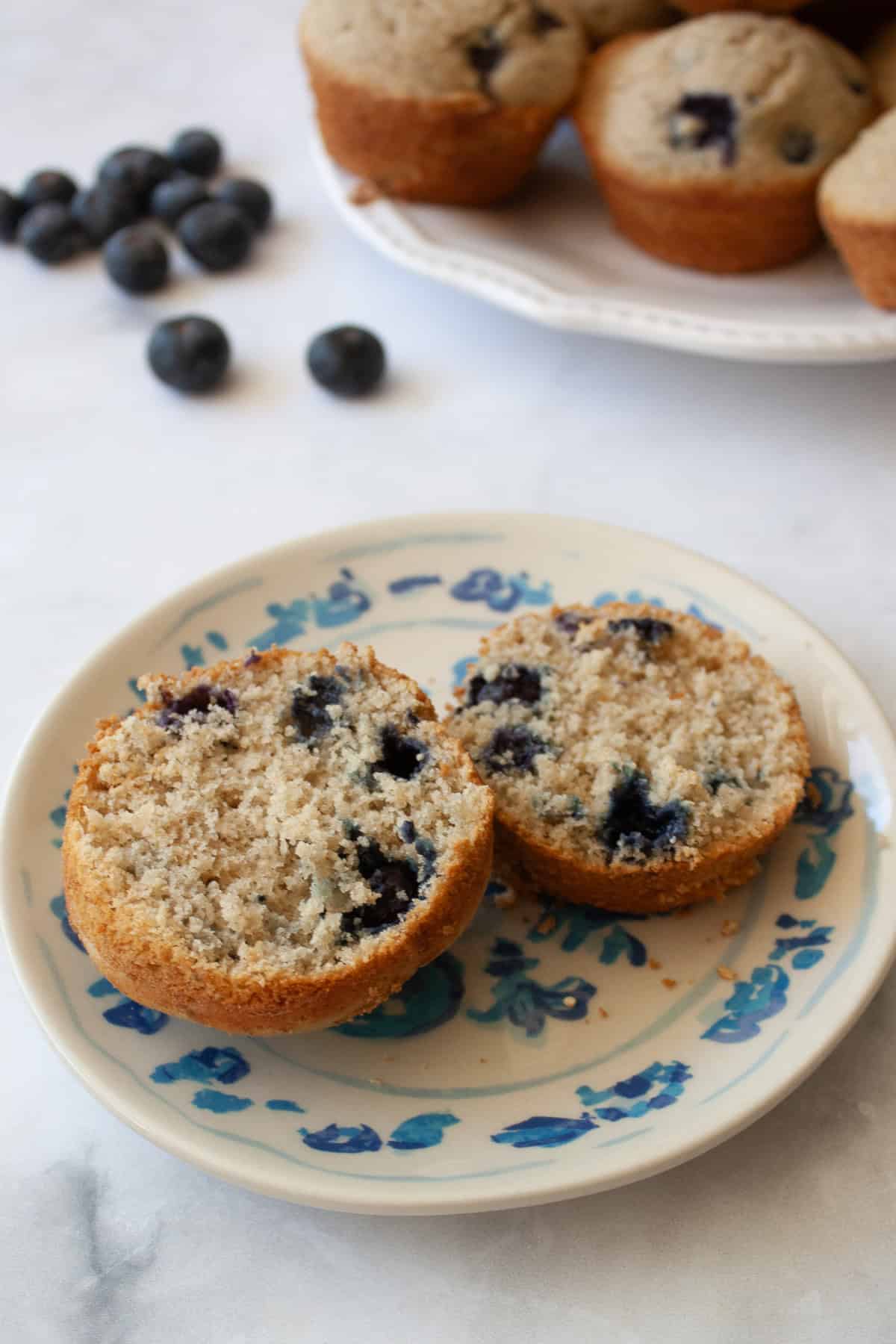 A whole wheat blueberry muffin cut in half on a plate.