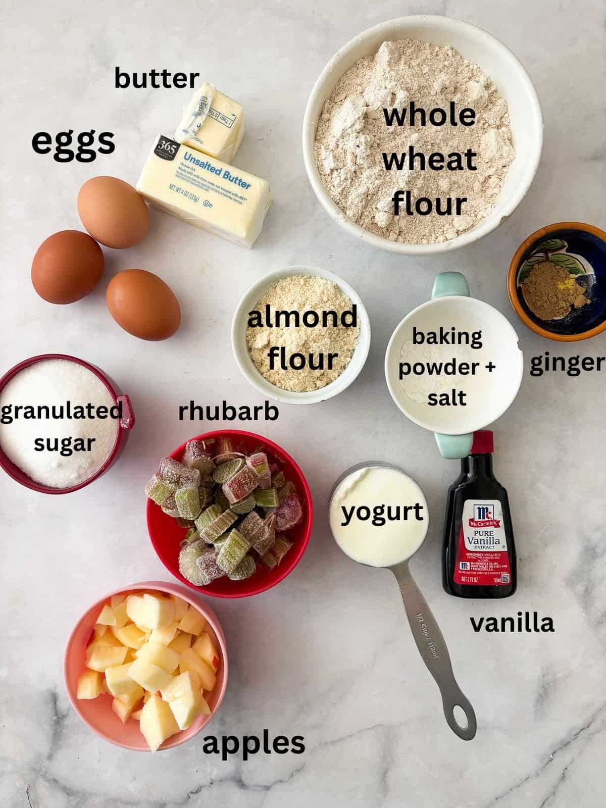 A nubbly and wholesome apple rhubarb cake that's made with whole-grain flour, yogurt, and plenty of juicy apples and tart rhubarb. Ingredients for apple rhubarb cake are text-labeled.