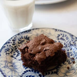 A glass of milk next to an almond flour brownie on a plate.