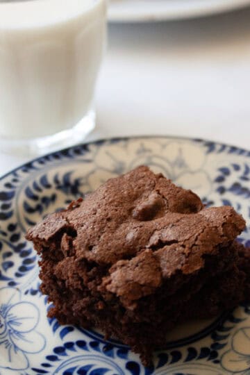A glass of milk next to an almond flour brownie on a plate.