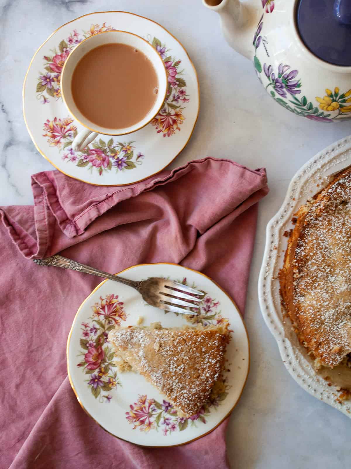 A nubbly and wholesome apple rhubarb cake that's made with whole-grain flour, yogurt, and plenty of juicy apples and tart rhubarb. A slice of apple rhubarb cake on a plate with a red napkin and a cup of tea.