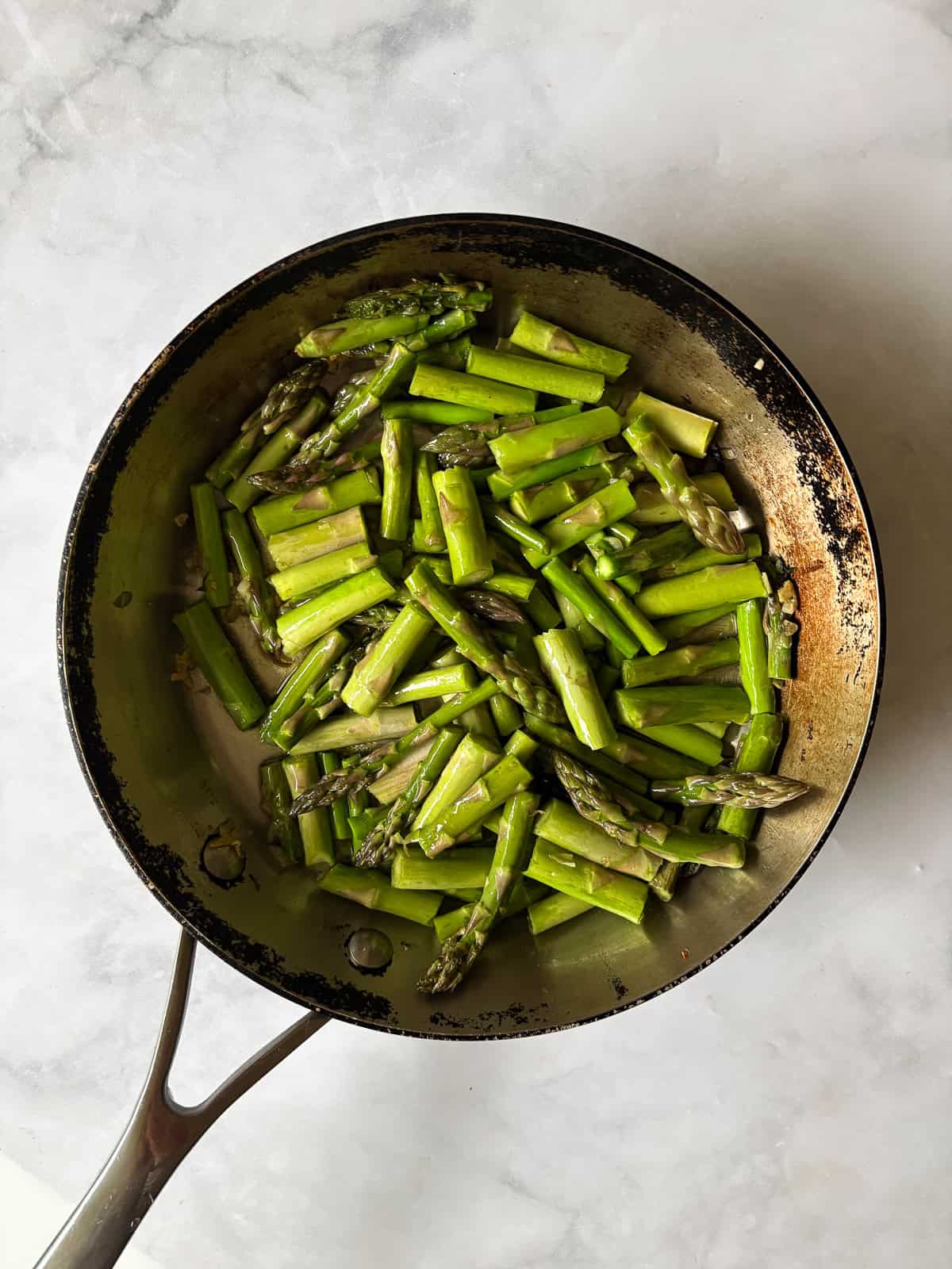 Cook to taste. I love that sweet spot between cooked through and still firm. You can cook the asparagus a bit more if you prefer softer asparagus and conversely, can cook it a little less for firmer asparagus. Herbs. Stir in some chopped fresh or dried herbs to the pan, such as parsley, basil, or oregano. Add more garlic. This recipe takes well to adjustments. Add more garlic if you like a lot of garlic. You can also use less. Serve cold. While I tend to serve this sautee with a hot meal, it's also lovely cold! You could mix it with quinoa and chickpeas to make a warm-weather side dish, or add leftover asparagus to a salad. Garlic is added to a skillet with asparagus.