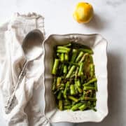 A white serving dish with asparagus and lemon and a serving spoon.