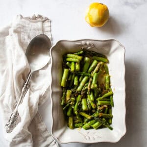 A white serving dish with asparagus and lemon and a serving spoon.