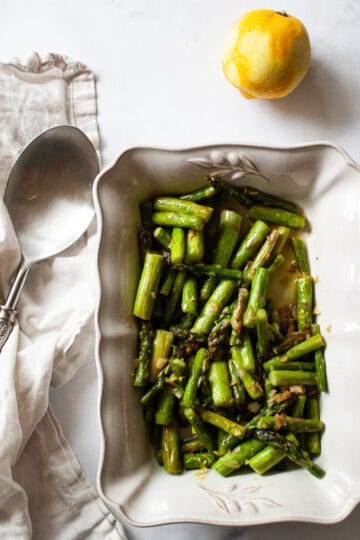 A white serving dish with asparagus and lemon and a serving spoon.