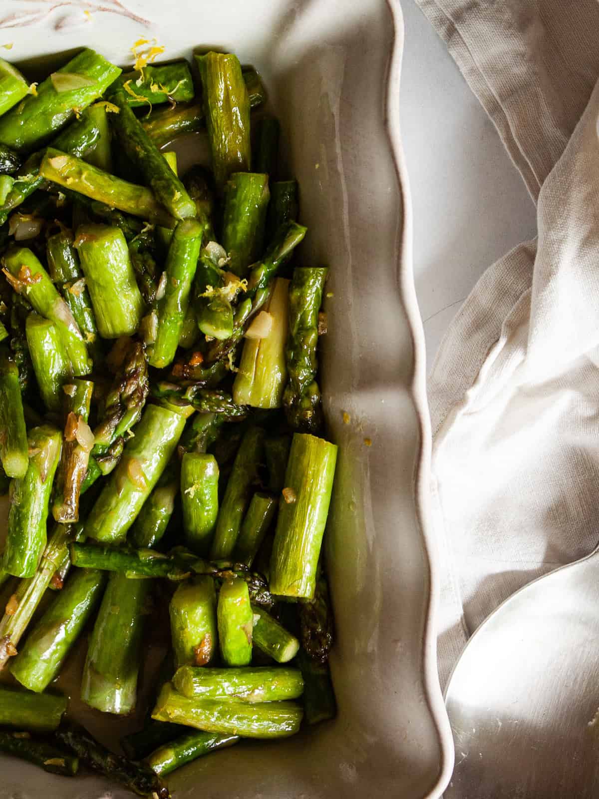 Cook to taste. I love that sweet spot between cooked through and still firm. You can cook the asparagus a bit more if you prefer softer asparagus and conversely, can cook it a little less for firmer asparagus. Herbs. Stir in some chopped fresh or dried herbs to the pan, such as parsley, basil, or oregano. Add more garlic. This recipe takes well to adjustments. Add more garlic if you like a lot of garlic. You can also use less. Serve cold. While I tend to serve this sautee with a hot meal, it's also lovely cold! You could mix it with quinoa and chickpeas to make a warm-weather side dish, or add leftover asparagus to a salad. Asparagus and lemon is shown close up in a serving dish.