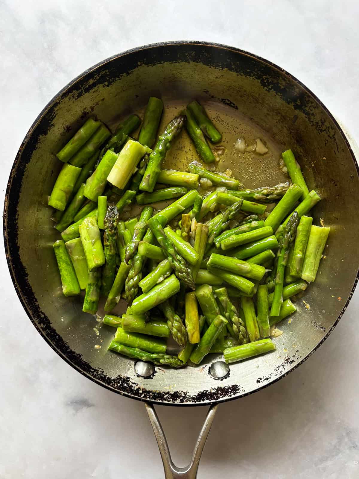 Cook to taste. I love that sweet spot between cooked through and still firm. You can cook the asparagus a bit more if you prefer softer asparagus and conversely, can cook it a little less for firmer asparagus. Herbs. Stir in some chopped fresh or dried herbs to the pan, such as parsley, basil, or oregano. Add more garlic. This recipe takes well to adjustments. Add more garlic if you like a lot of garlic. You can also use less. Serve cold. While I tend to serve this sautee with a hot meal, it's also lovely cold! You could mix it with quinoa and chickpeas to make a warm-weather side dish, or add leftover asparagus to a salad. The finished skillet of sauteed asparagus and lemon.
