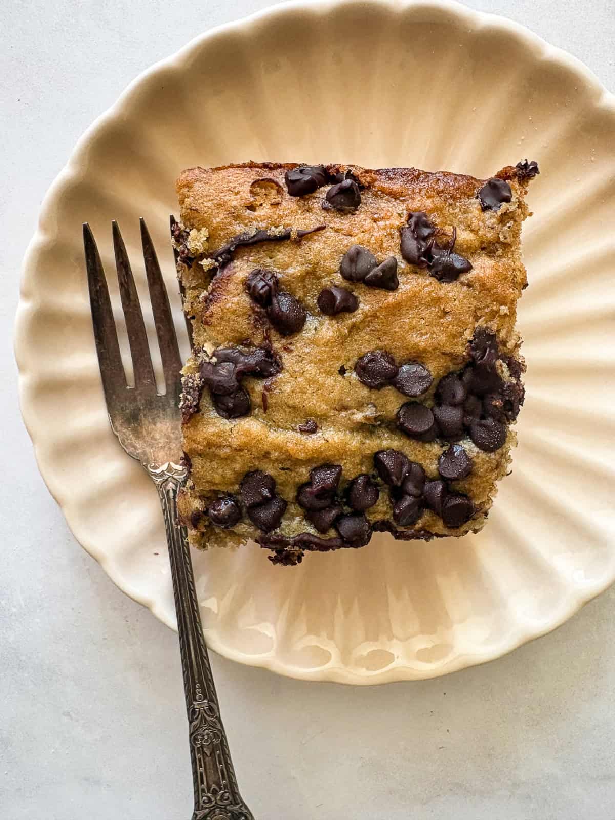 A fork rests next to a square of banana snack cake on a plate.