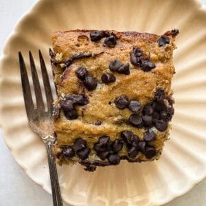 A fork rests next to a square of banana snack cake on a plate.