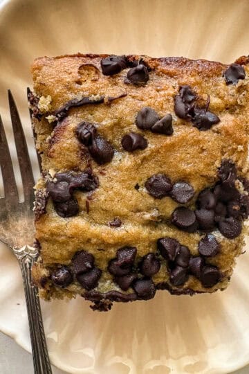 A fork rests next to a square of banana snack cake on a plate.