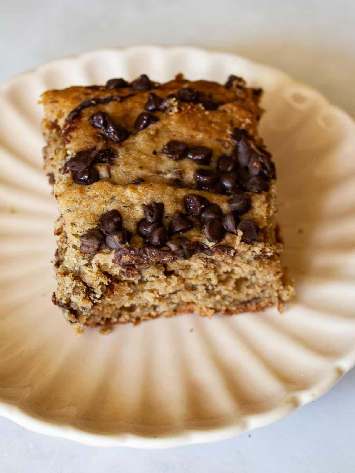 This banana snack cake is fluffy, moist, and balanced by warming spices. Naturally gluten-free, or make it with whole wheat flour. Chocolate chips scattered over the top of a slice of banana snack cake.