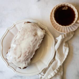 A loaf of cherry bread with lemon glaze next to a napkin and a cup of tea.