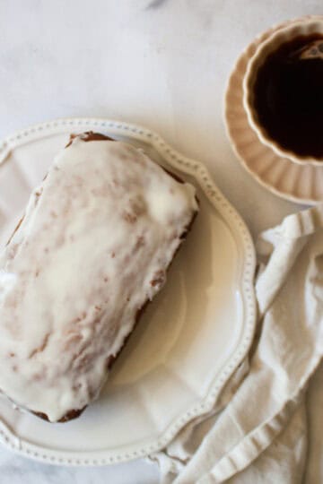 A loaf of cherry bread with lemon glaze next to a napkin and a cup of tea.