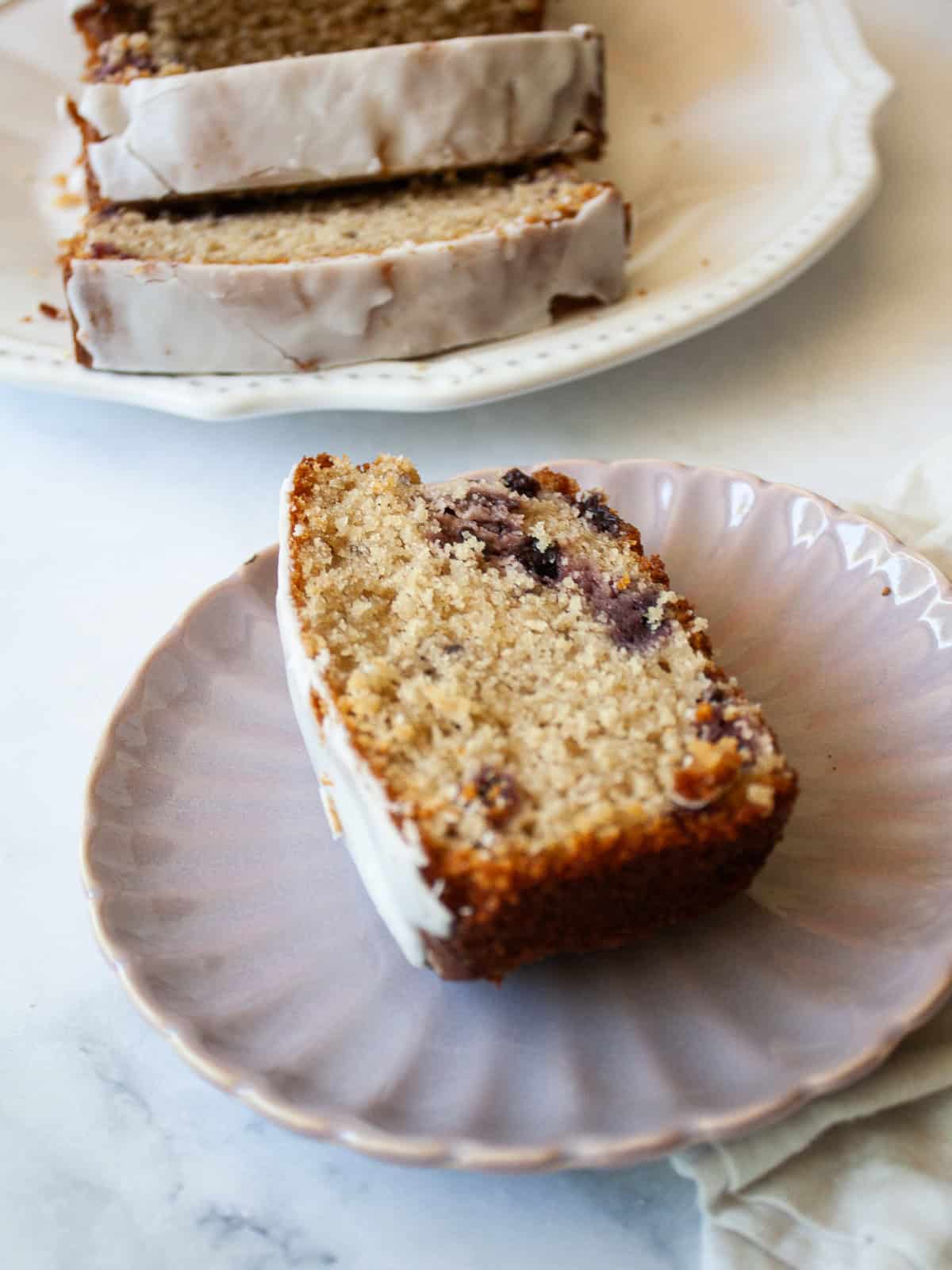 This pretty cherry bread is made in just one bowl and is finished with a lemon glaze. Whole grain flour, Greek yogurt - all the good stuff! A slice of cherry bread with lemon glaze on a purple plate.