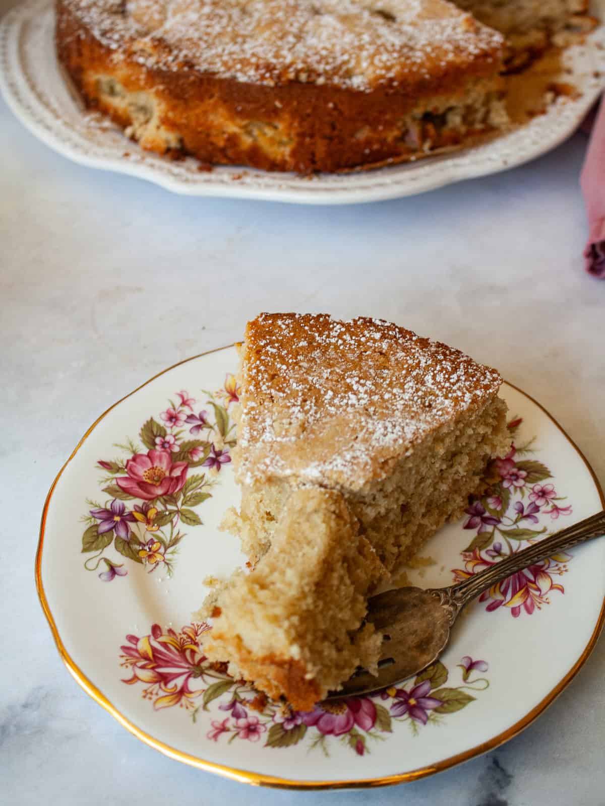 This pretty cake marries crisp, sweet apples with tart rhubarb to make a seasonal gluten free apple and rhubarb cake! A fork cuts into a s lice of apple and rhubarb cake.