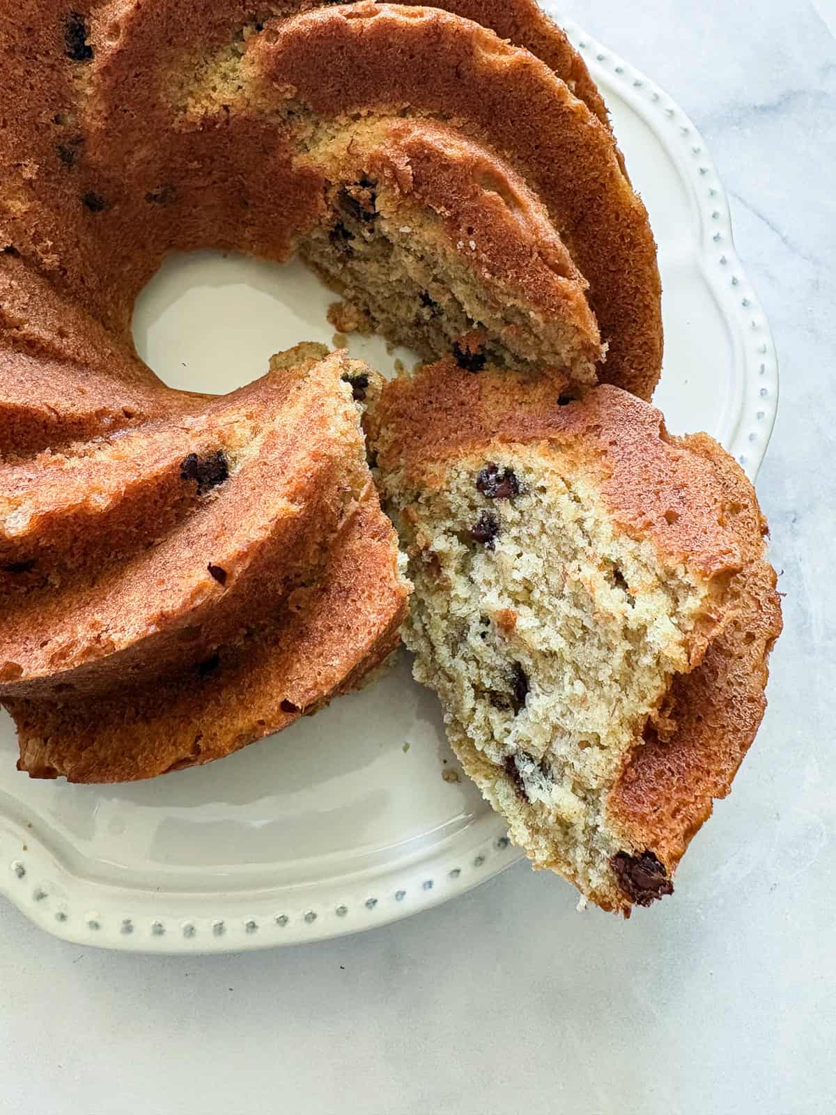 A slice of banana bundt cake is pulled from the cake.