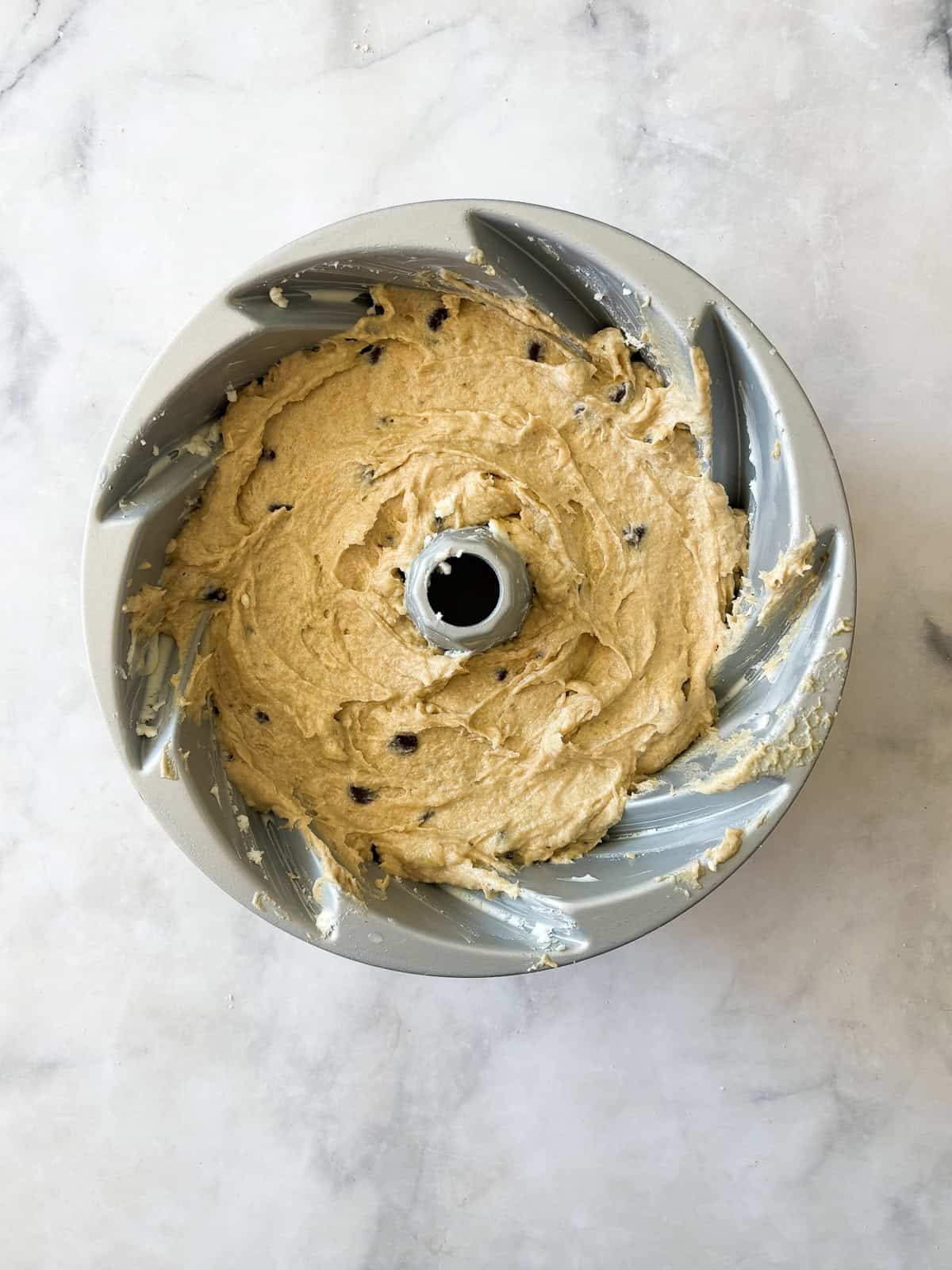 This rich, gluten free banana bundt cake is made with plenty of butter and sugar, then swirled with bananas and chocolate chips. Batter for gluten free banana bundt cake in a pan.
