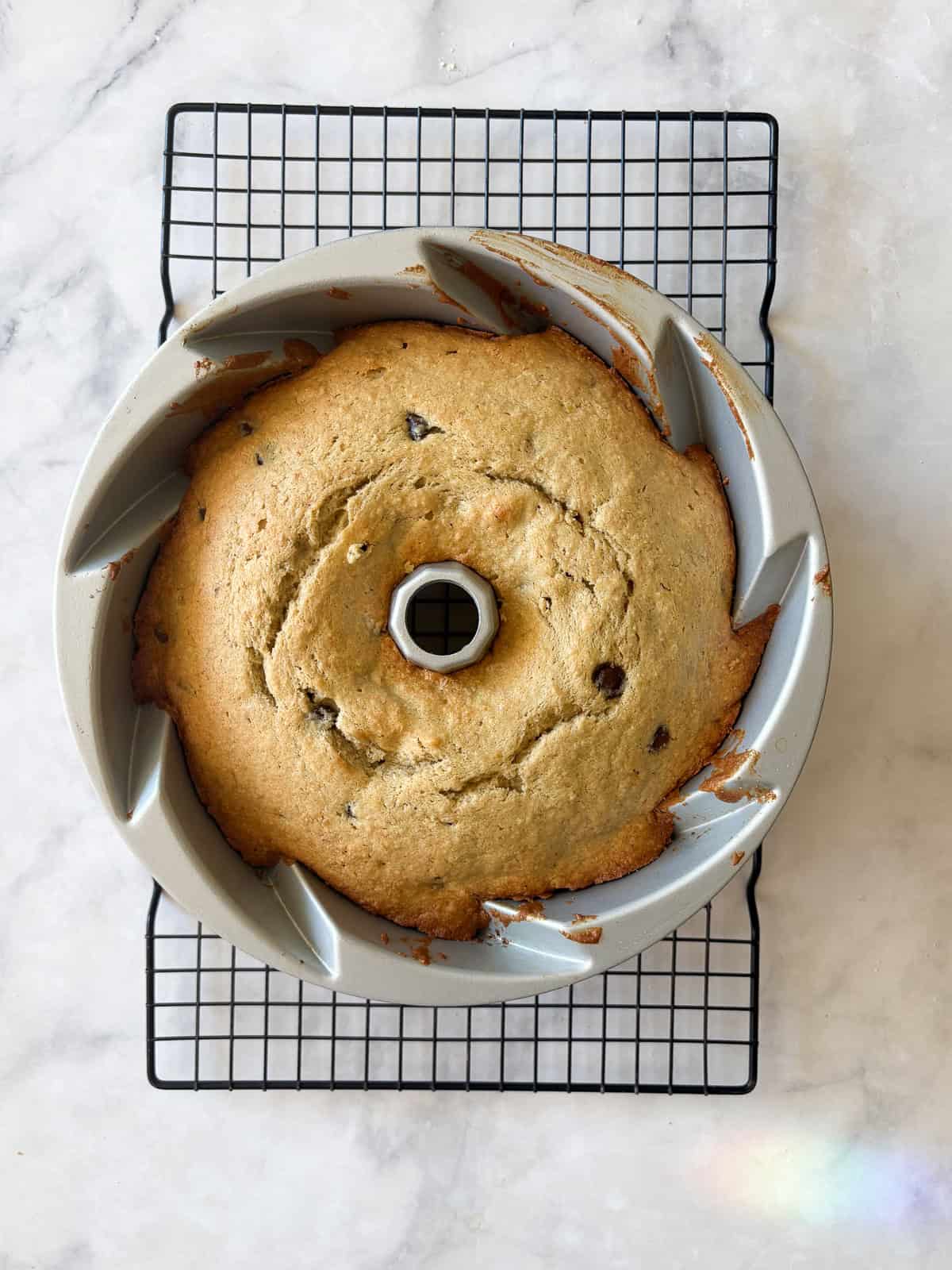 This rich, gluten free banana bundt cake is made with plenty of butter and sugar, then swirled with bananas and chocolate chips. A baked gluten free banana bundt cake cools.