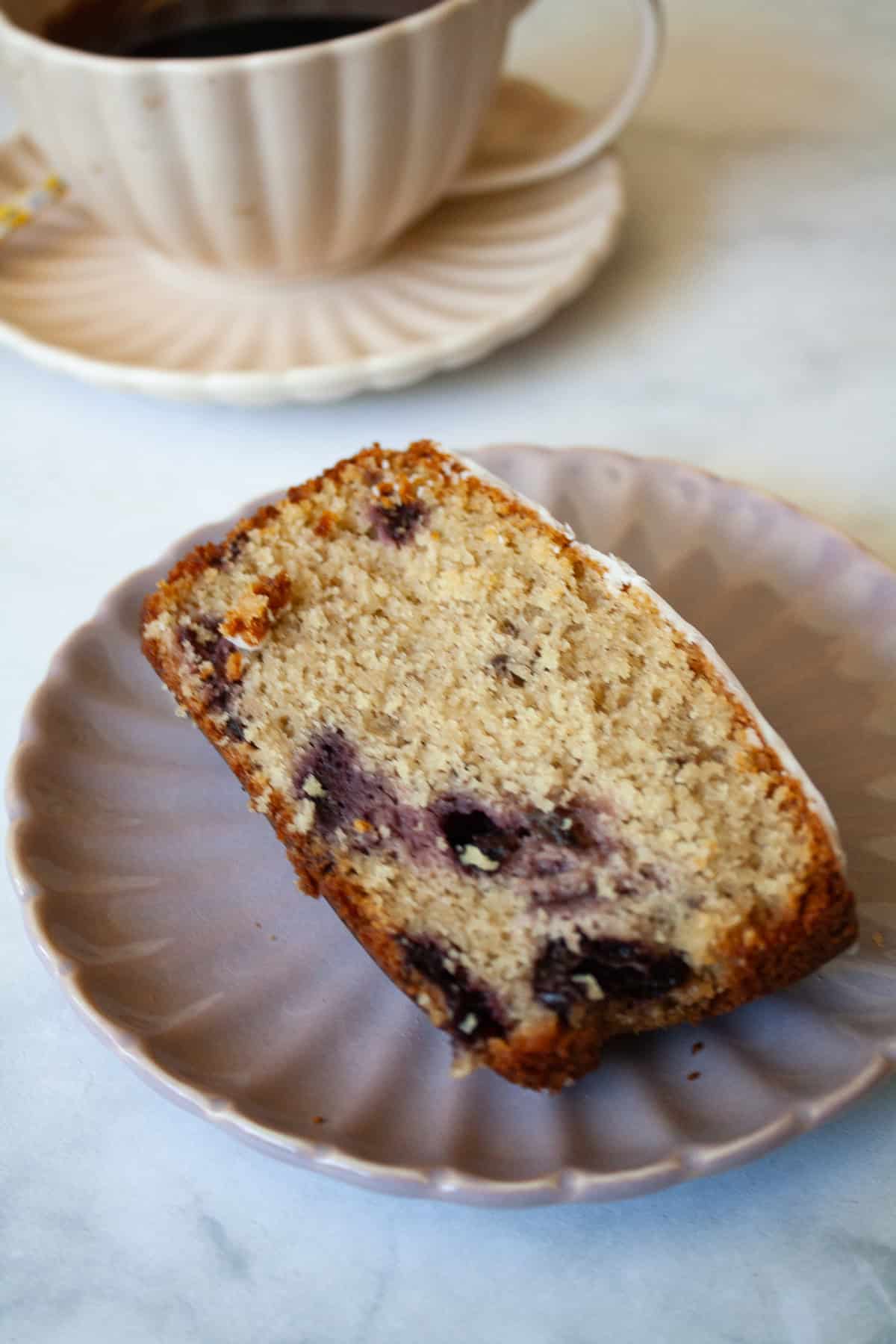 A recipe for a one-bowl gluten free cherry loaf cake that's swirled with chopped cherries and finished with a slick of tart lemon glaze. A slice of gluten free cherry loaf cake o a plate.