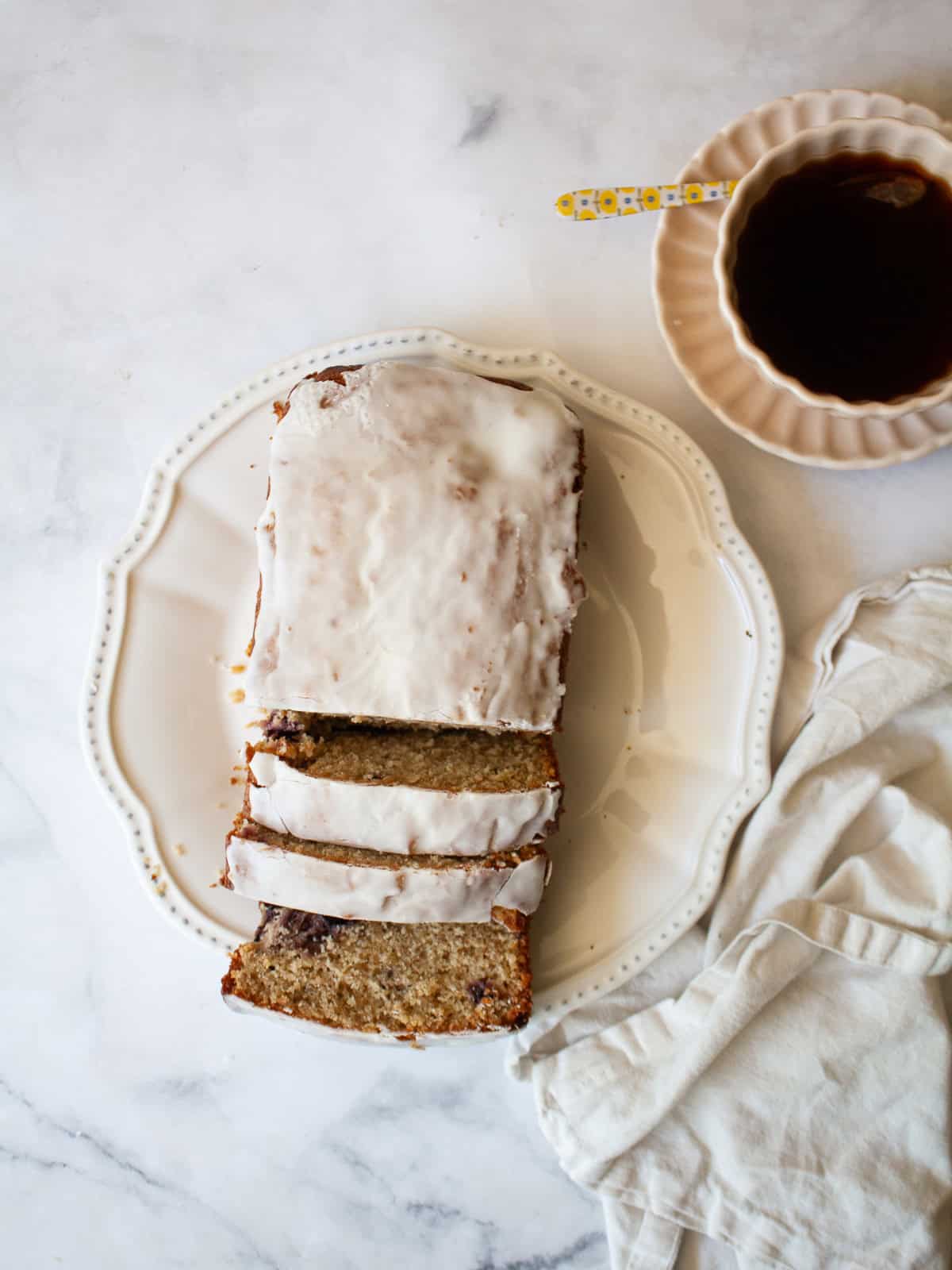 A recipe for a one-bowl gluten free cherry loaf cake that's swirled with chopped cherries and finished with a slick of tart lemon glaze. A sliced loaf of gluten free cherry loaf cake next to a cup of tea.