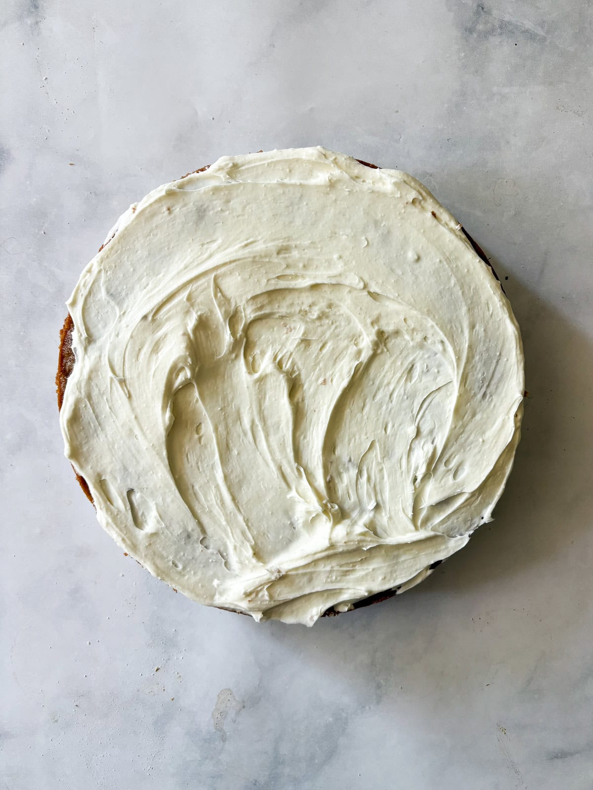 This gluten-free hummingbird cake is a moist, fruit-infused cake topped with tangy cream cheese icing and sprinkled with toasted walnuts. Adding cream cheese frosting to a gluten fre hummingbird cake cake layer.