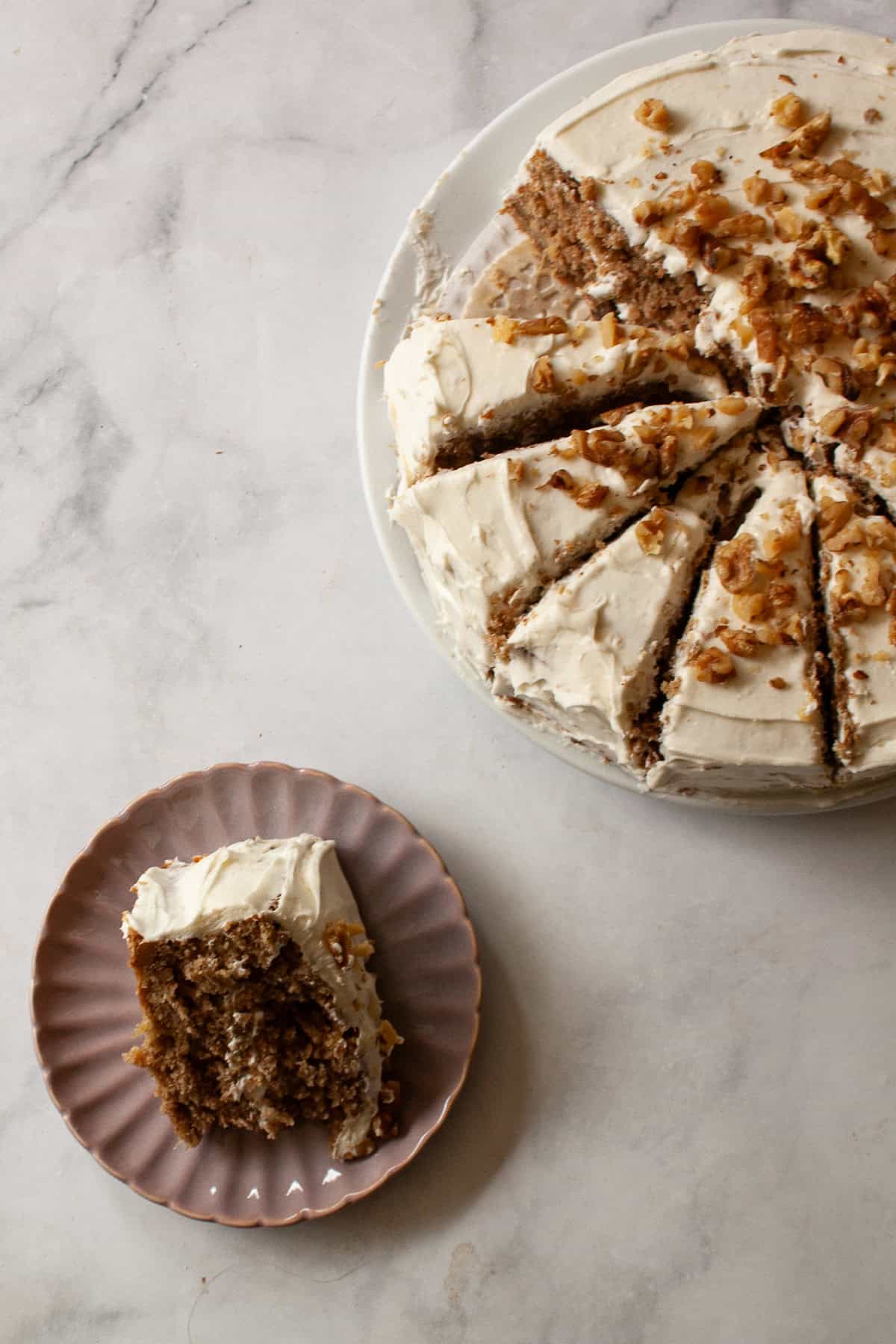 This gluten-free hummingbird cake is a moist, fruit-infused cake topped with tangy cream cheese icing and sprinkled with toasted walnuts. A slice of gluten free hummingbird cake on a plate next to the cake.