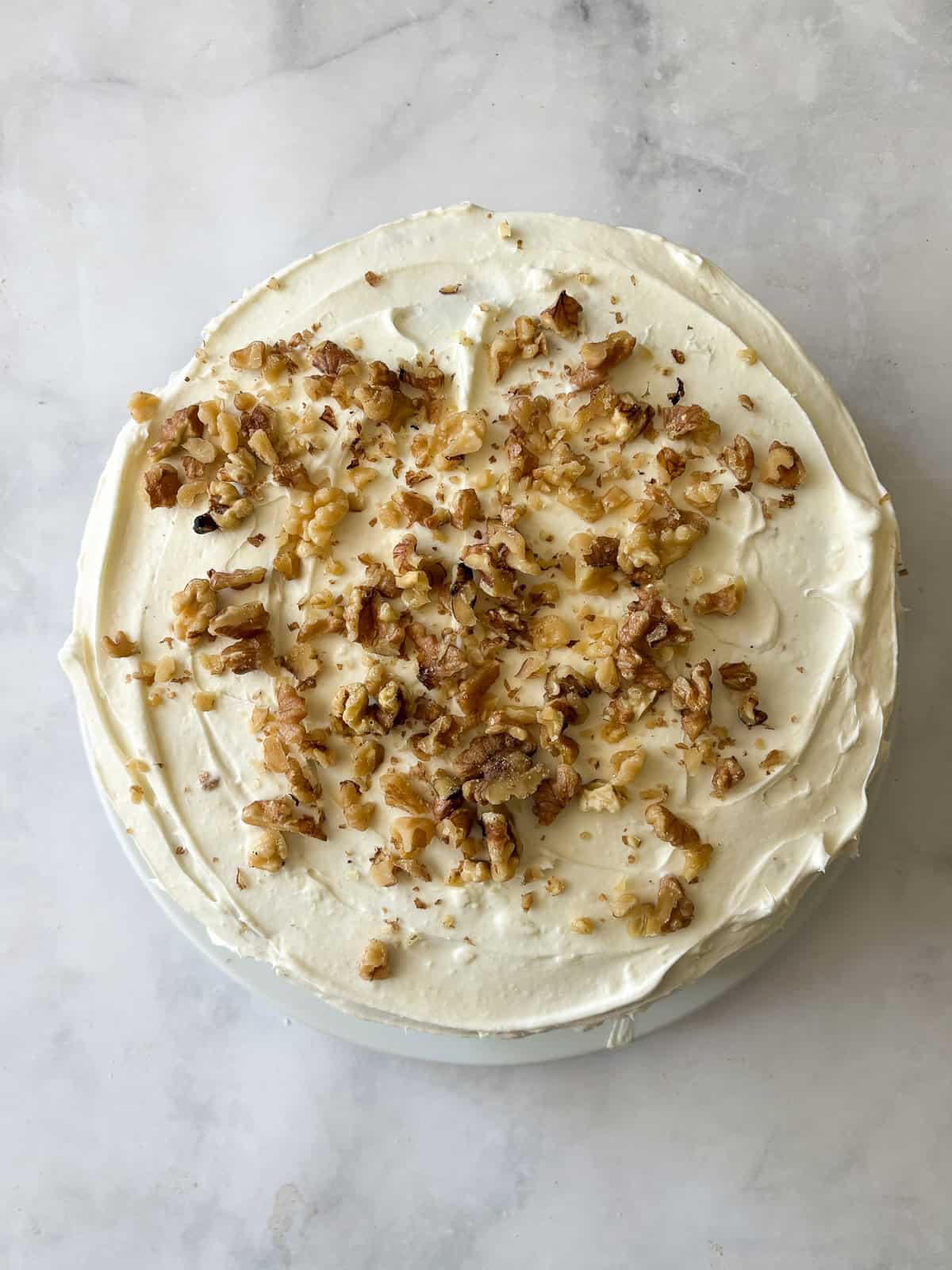 This gluten-free hummingbird cake is a moist, fruit-infused cake topped with tangy cream cheese icing and sprinkled with toasted walnuts. A gluten free hummingbird cake is topped with walnuts.