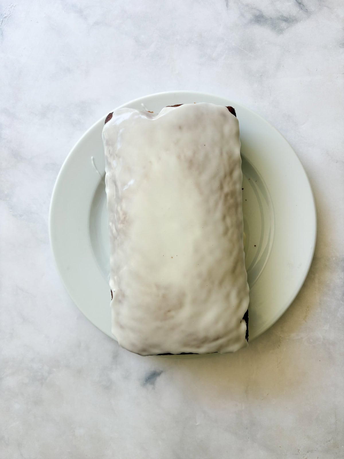 Lemon icing is added to a loaf of gluten free lemon blueberry bread.