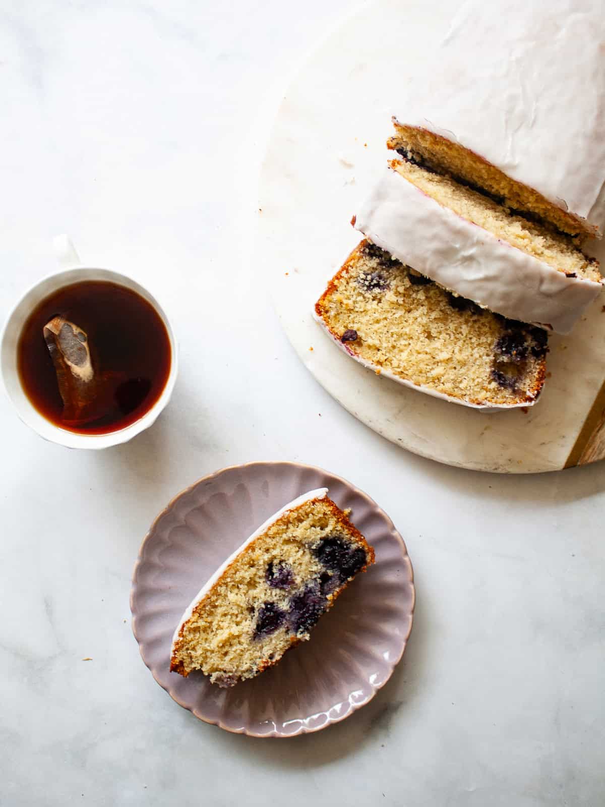 A cup of tea, a slice of lemon blueberry loaf on a plate, and the sliced loaf.