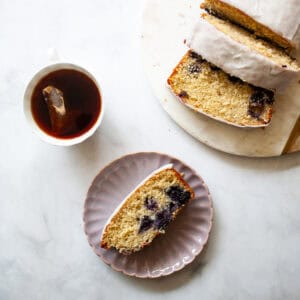 A cup of tea, a slice of lemon blueberry loaf on a plate, and the sliced loaf.