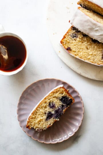 A cup of tea, a slice of lemon blueberry loaf on a plate, and the sliced loaf.