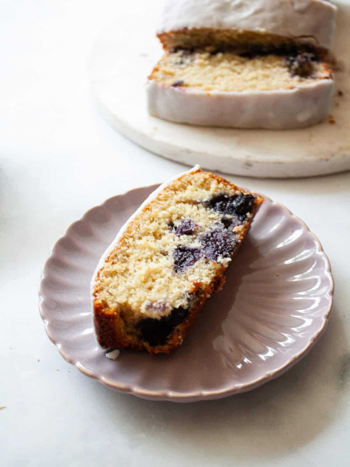 A slice of gluten free lemon blueberry bread on a plate next to the loaf.