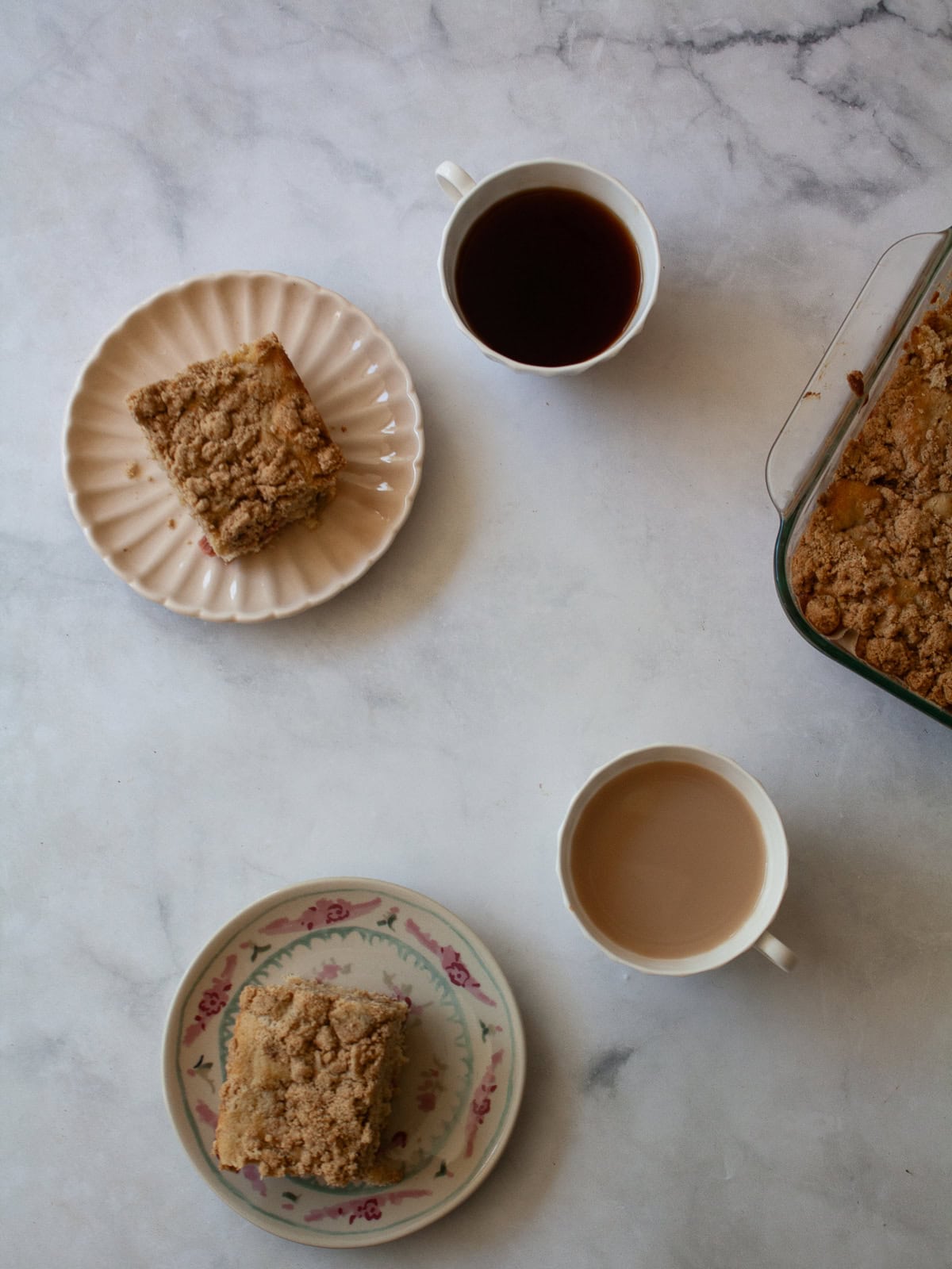 A soft and sweet gluten free rhubarb crumb cake with tart bits of rhubarb and a buttery, brown sugar streusel. Great for brunch! Cups of tea and slices of gluten free rhubarb crumb cake with the cake next to them.