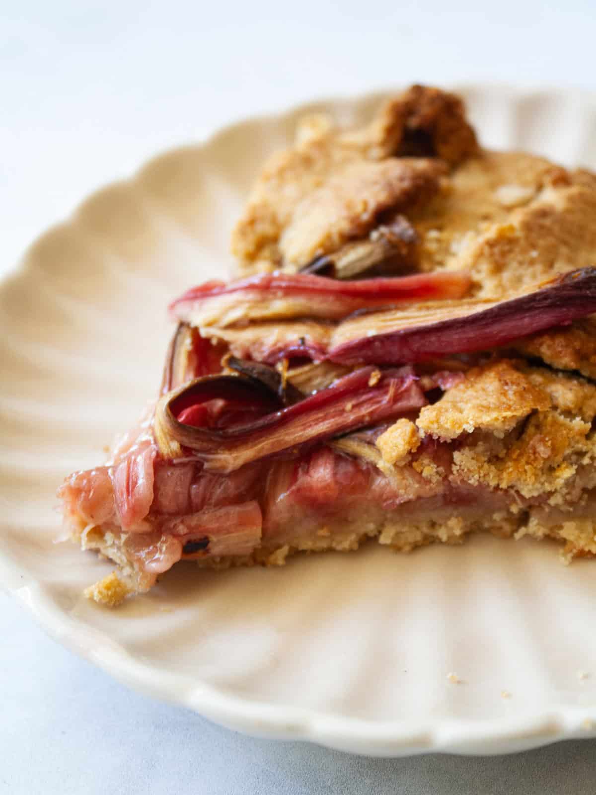 A tender and flaky gluten-free pastry wraps around sweet-tart slices of rhubarb in this rustic gluten free rhubarb galette. A slice of gluten free rhubarb galette on a plate.