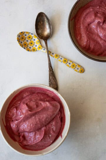 Two bowls of homemade Greek frozen yogurt and two spoons.