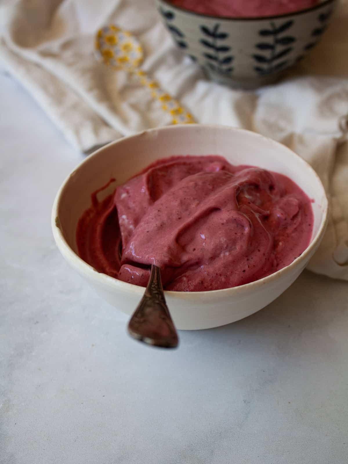 Just two ingredients - fruit and yogurt - plus a food processor are needed to make this refreshing and easy homemade Greek frozen yogurt. A bowl of homemade Greek frozen yogurt with a spoon in it.