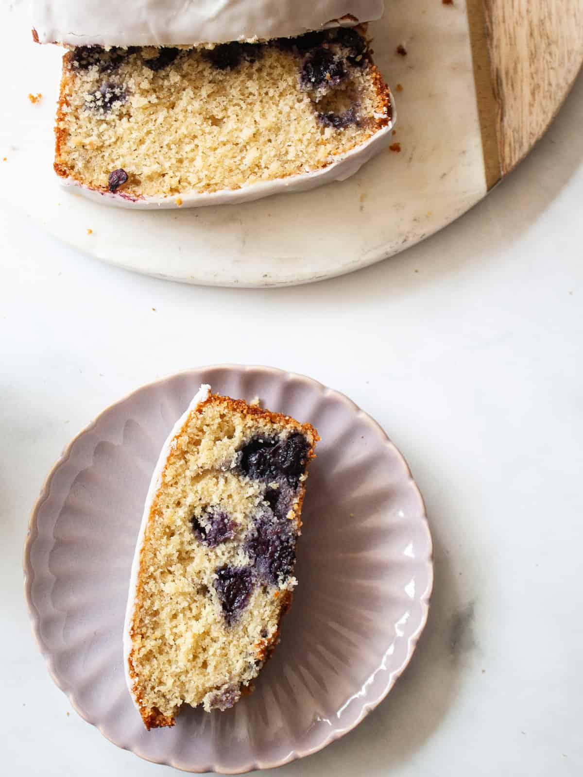 A soft and sweet lemon blueberry loaf that's studded with juicy fruit and topped with a lusciously thick, lemon-spiked glaze. A slice of lemon blueberry loaf on a plate next to the sliced loaf.