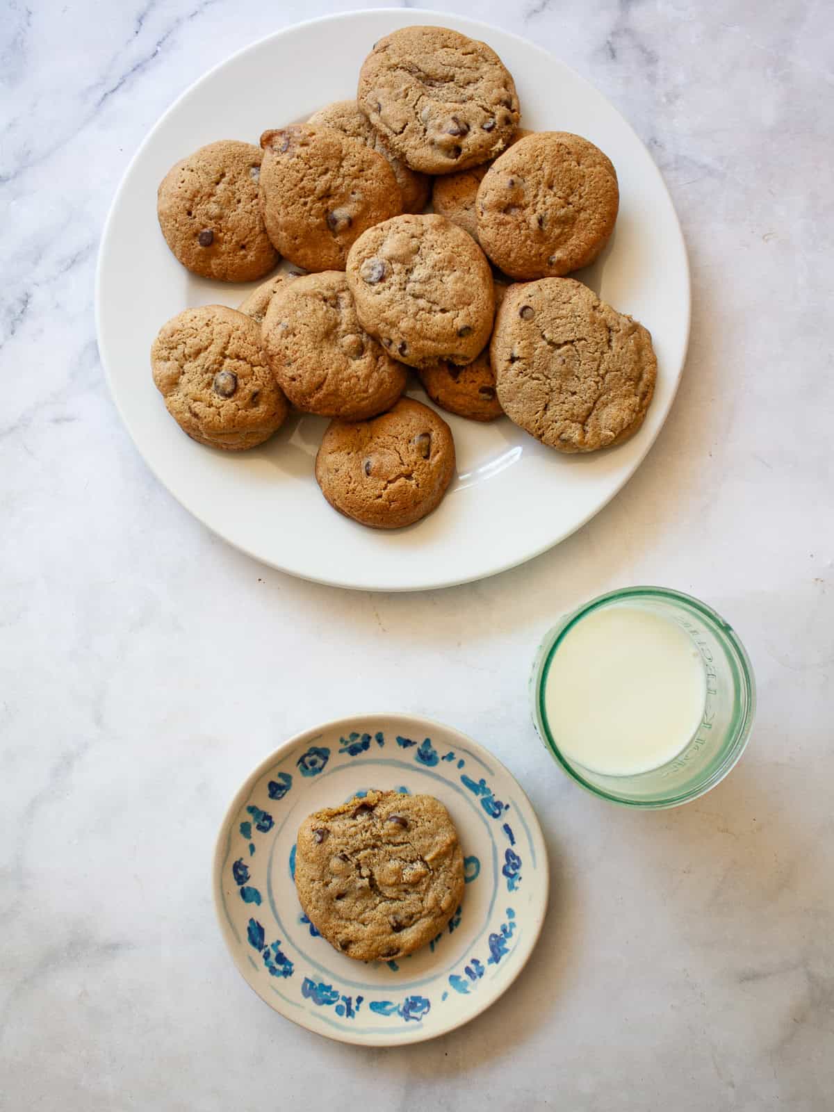 One of my favorite types of cookies, these maple chocolate chip cookies are sweetened with a combination of maple syrup and brown sugar. A plate of maple syrup chocolate chip cookies, a cookie on a plate, and a glass of milk.