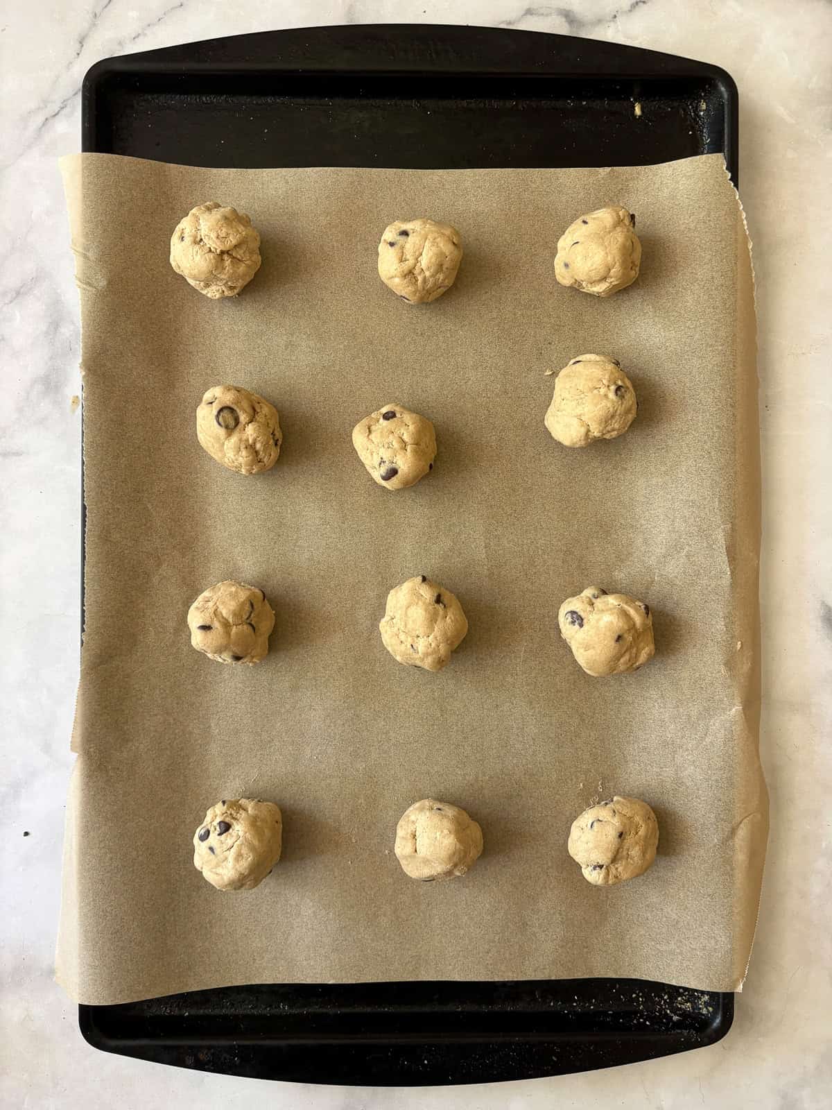 One of my favorite types of cookies, these maple chocolate chip cookies are sweetened with a combination of maple syrup and brown sugar. Balls of maple syrup chocolate chip cookie dough on a baking sheet.