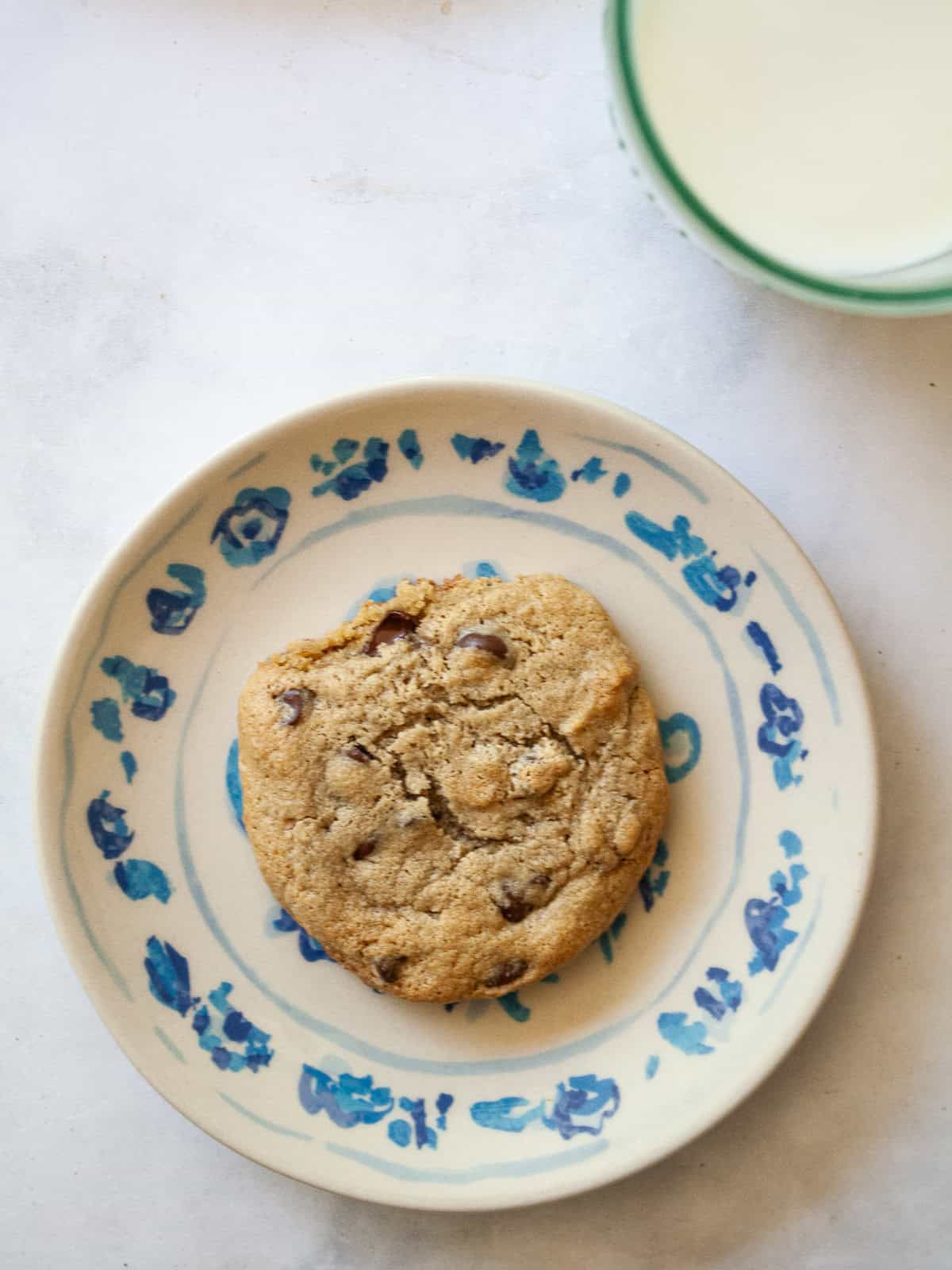 A maple syrup chocolate chip cookie on a plate with a glass of milk behind it.