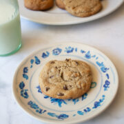 A glass of milk next to a plate with a maple syrup chocolate chip cookie.
