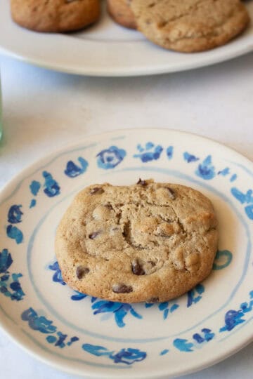 A glass of milk next to a plate with a maple syrup chocolate chip cookie.