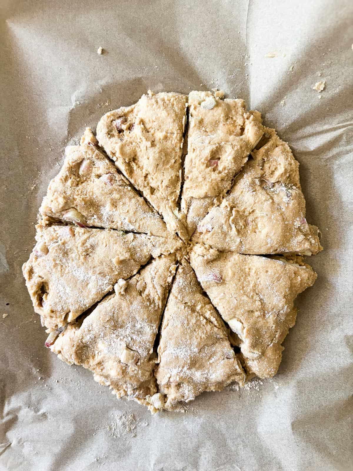 Whole-grain oat flour rhubarb scones are naturally gluten-free, warmed with a bit of orange zest and studded with jammy pockets of rhubarb. Oat flour rhubarb scones dough is cut into wedges on a baking sheet.
