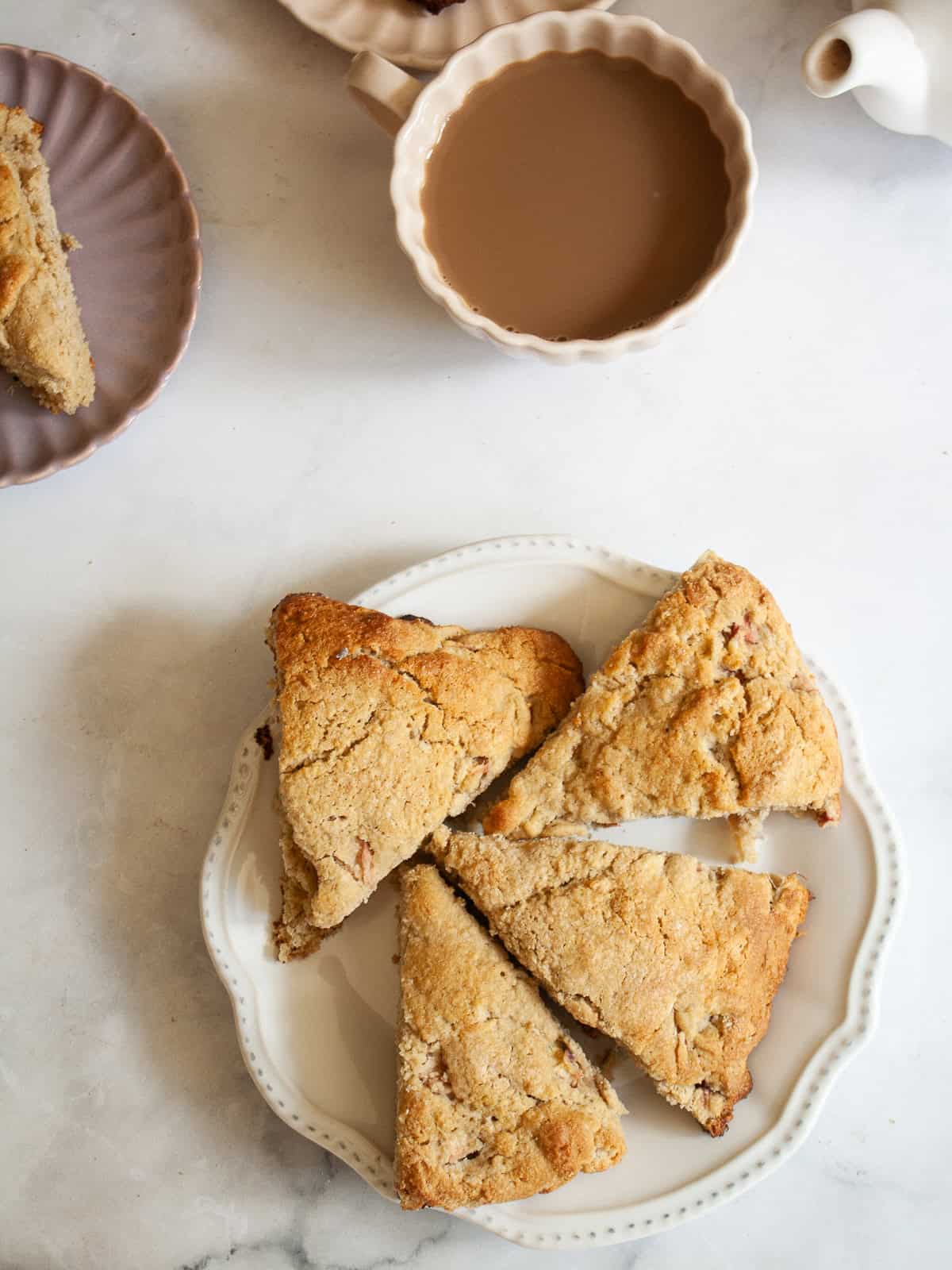 Whole-grain oat flour rhubarb scones are naturally gluten-free, warmed with a bit of orange zest and studded with jammy pockets of rhubarb. A plate of oat flour rhubarb scones next to a pot of tea.