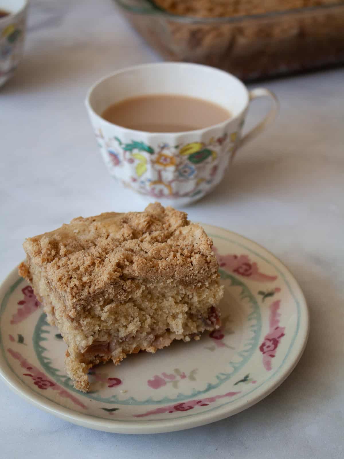 This rhubarb crumb cake is studded with jammy bits of tart rhubarb and topped with a cinnamon-laced brown sugar streusel. A cup of tea next to a slice of rhubarb crumb cake on a plate.
